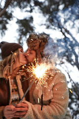 young couple kissing and holding sparklers on a background of snow-covered park and trees, loving couple, smiles on their faces, magical winter, on the eve of Valentine's Day.