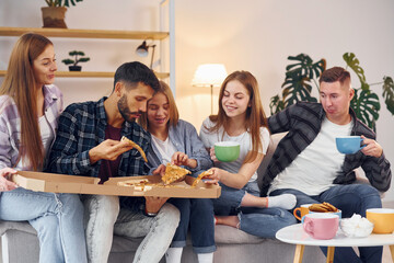 With cups of drink. Group of friends have party indoors together
