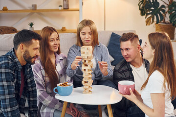Playing wooden tower game. Group of friends have party indoors together