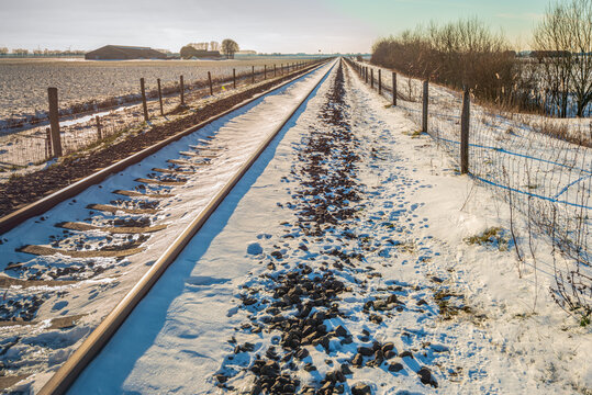 Single track train rails in a snowy polder landscape. The photo was taken on a winter day near the village of Hooge Zwaluwe in the Dutch province of North Brabant.