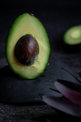 Two halves of fresh avocado on dark stone background .