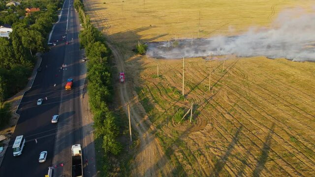 Red firetruck go straight to epicenter of agricultural field fire with smoke near highway with lot of cars. Emergency case for danger mission and rescue nature saving concept