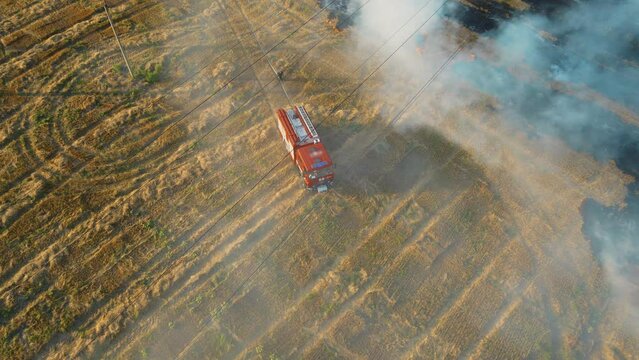 Brave firefighters rush to fight burning flame on agronomic field with clouds of smoke and fire truck with water driving by danger dry stubble. Emergency case for danger mission and rescue nature