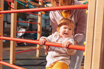 Obraz premium A little pretty child climbs the children's sports wall with the help of his mother. The concept of children's games and development