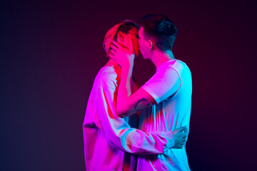 Closeup two young men, couple kissing isolated on blue background in neon light. Concept of emotions, love, relations, human rights