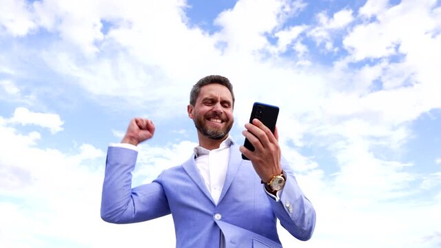 Excited euphoric broker winner looking at smartphone making winning gesture on sky, mobile bet