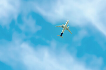 Commercial airplane flying against blue cloudscape sky. Jet plane in high flight. Airliner flying under the clouds. Aircraft flying in the clouds. Bottom view