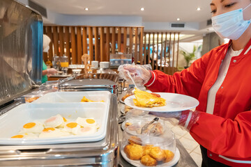 A woman in a protective medical mask collects food for breakfast in the buffet of her hotel, observing all coronavirus restrictions