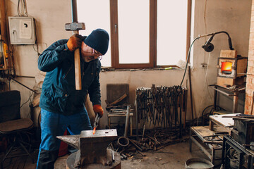 Blacksmith forges and makes metal detail with hammer and anvil at smith farrier forge.
