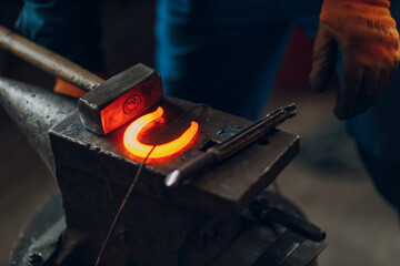 Blacksmith forges and making metal horseshoe with hammer and anvil at forge.