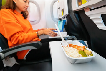 Happy woman ordered tasty dish during the flight in the plane and eats fish with rice. Catering and menu on the airplane