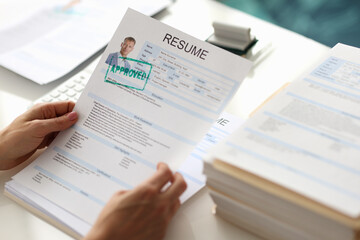 Fototapeta na wymiar Hands holding resume of man for employment with stamp approved closeup