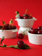Close up of a cherry in front of bowls of cherries, on red background
