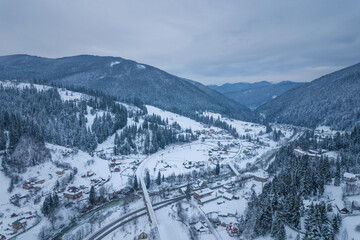 A valley with a village surrounded by mountains and forest. Gloomy winter weather.