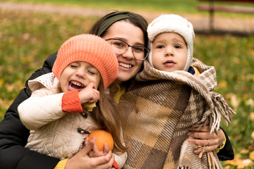 Obraz premium Young Woman Mom And Little Cute Preschool Minor Children In Orange Plaid At Yellow Fallen Leaves Nice Smiling Look At Camera In Cold Weather In Fall Park. Childhood, Family, Motherhood, Autumn Concept