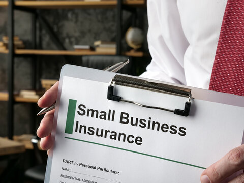 Hand holds clipboard with application small business insurance.