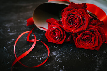 Bouquet of dark red roses for valentine's day with ribbon on black stone slab. Background for...