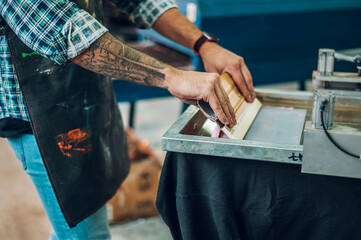 Male worker pressing ink on frame while using the printing machine in a workshop