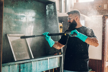 Male worker cleaning screen frame with water in a printing workshop