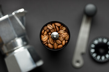 Coffee grinder with coffee beans and coffee maker on gray background top view. Beans in focus, coffee setup with background blurred. - obrazy, fototapety, plakaty