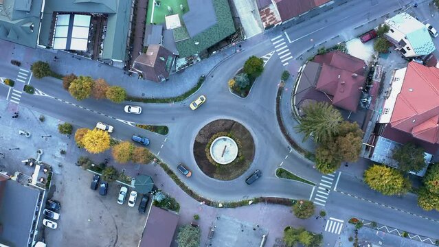 Aerial top down 4k view of car driving on roundabout in a small romanian town. Cinematic drone shot flying over gravel road in pine tree forest. aerial view 