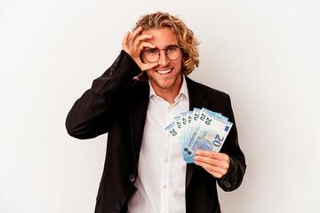 Young caucasian business man holding banknotes isolated on white background excited keeping ok gesture on eye.