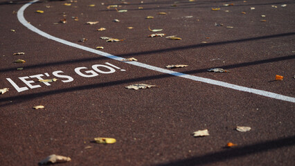 Sign Let's go. Empty sports field with running track markings used in outdoor tennis in autumn with...