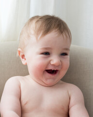 Medium vertical photo of adorable blue-eyed bare-chested toddler boy sitting in armchair laughing