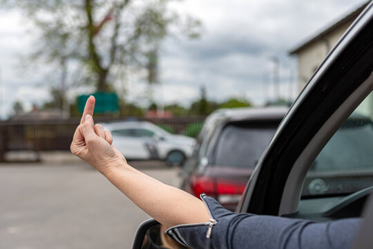 woman shows obscene gesture from a car, rude and furious driver giving middle finger to car behind