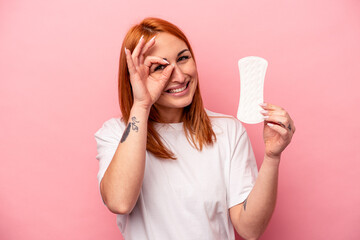 Young caucasian woman holding sanitary napkin isolated on pink background excited keeping ok gesture on eye.