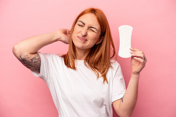 Young caucasian woman holding sanitary napkin isolated on pink background touching back of head, thinking and making a choice.