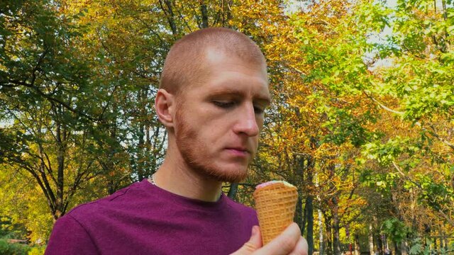 Red-haired beautirful man caucasian eating ice cream cone in Park