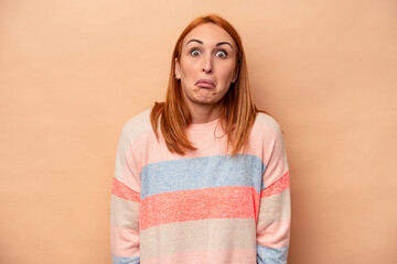 Young caucasian woman isolated on beige background shrugs shoulders and open eyes confused.