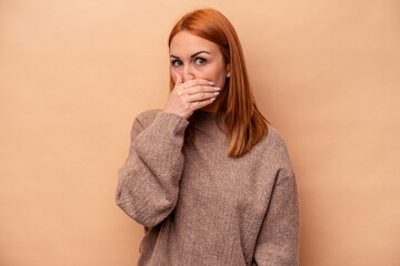 Young caucasian woman isolated on beige background covering mouth with hands looking worried.