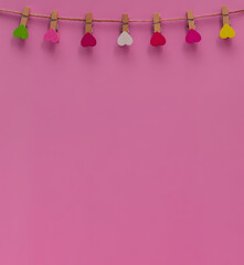 Wooden clothespins with colorful hearts on a rope on a pink background. Composition for Valentine's Day. Flat lay, copy space. Greeting card. 