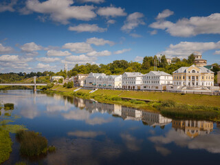 Fototapeta na wymiar summer travel to Russia, Torzhok city, Tver region. View on old buildings at the embankment from the bridge across the Tvertsa river. Rural landscape