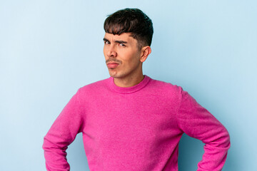 Young mixed race man isolated on blue background frowning face in displeasure, keeps arms folded.