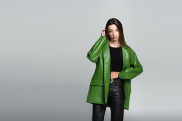 pretty woman in green jacket and black trousers standing with hand on waist isolated on grey.