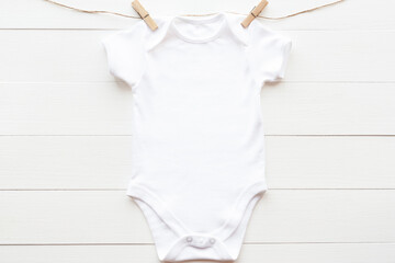 Mockup of white baby bodysuit on wood background with clothespins and rope, flat lay. Blank gender...