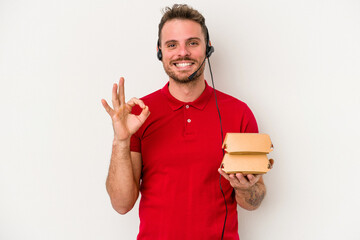 Young caucasian delivery man holding a burger isolated on white background cheerful and confident...