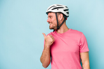Young caucasian man with bike helmet isolated on blue background points with thumb finger away, laughing and carefree.