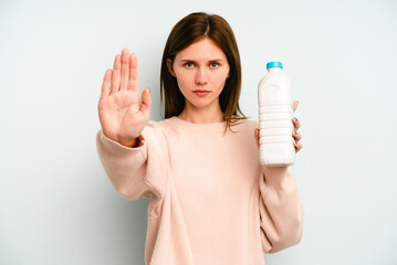 Young English woman holding a bottle of milk isolated on blue background standing with outstretched hand showing stop sign, preventing you.