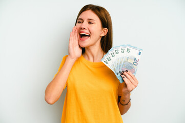 Young English woman holding banknotes isolated on blue background shouting and holding palm near opened mouth.