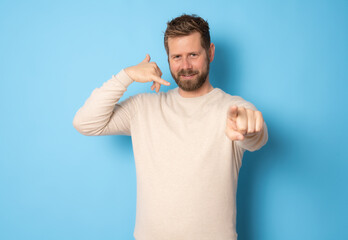 Fototapeta premium Young bearded man making call me gesture standing isolated over blue background.
