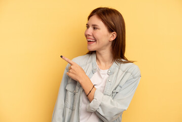 Young English woman isolated on yellow background looks aside smiling, cheerful and pleasant.