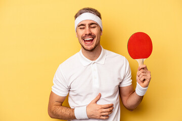 Young caucasian man holding ping pong rackets isolated on yellow background laughing and having fun.