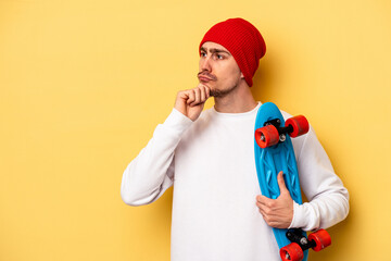 Young skater caucasian man isolated on yellow background looking sideways with doubtful and...