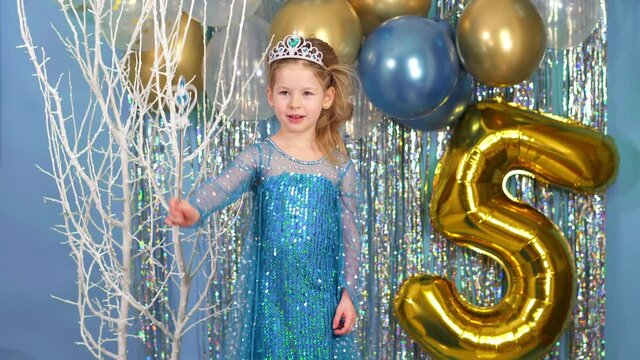  girl waves a magic wand and makes a wish in dress and with crown. Little princess on birthday. 5 years and tinsel. Little princess sings song in the studio. Halloween image from cold heart.