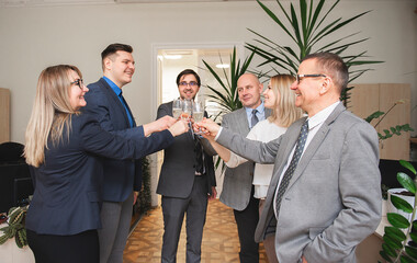 Successful business people are clinking glasses of champagne and smiling while celebrating in office