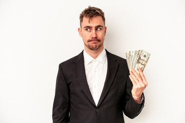 Young caucasian business man holding bank notes isolated on white background confused, feels doubtful and unsure.